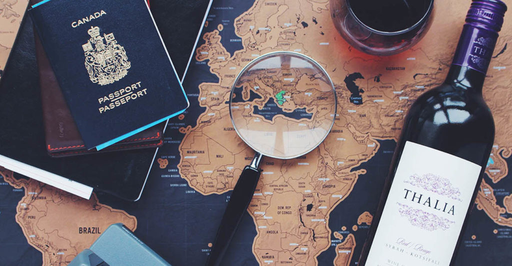 Bild zeigt einen Reisepass, eine Flasche Wein, EIne Lupe und eine Weltkarte